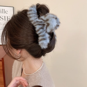 Detail of blue plush hair claw clip with brown stripes worn by model in cozy home setting