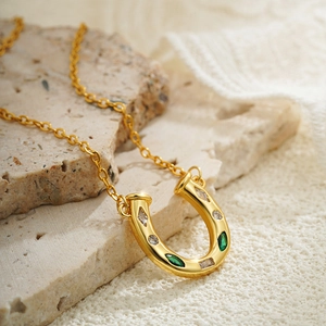 18K gold horseshoe necklace with white and green stones on a marble block backdrop