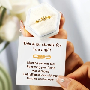 Gros plan d'une bague nœud doré avec zircon dans un écrin blanc avec carte de message