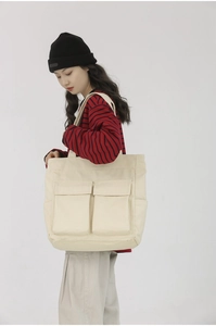 Detail of beige canvas tote bag with front flap pockets shown on a model