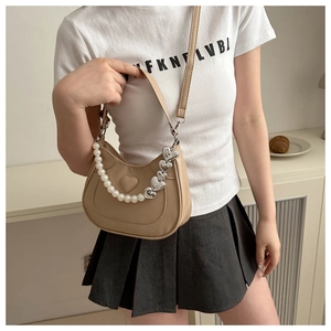 Detailed view of beige half-moon crossbody bag with pearl chain and heart embossing