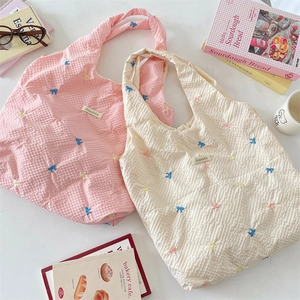 Detail view of pink and beige canvas tote bags with colorful bow embroidery and brand label