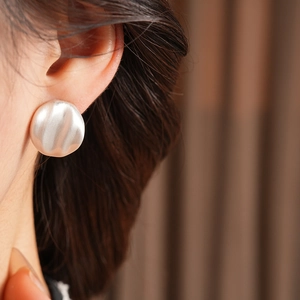 Detail of silver geometric stud earring with brushed texture worn by a model