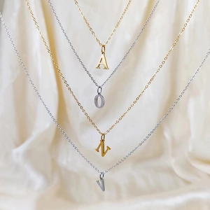 Detailed view of gold and silver initial necklaces A O N V on soft cream silk fabric
