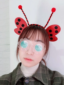 Detail of red ladybug headband with black dots and transparent flower glasses on a model
