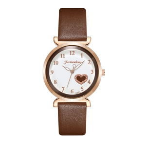 Detail of rose gold watch case with brown leather strap and heart-shaped dial cutout