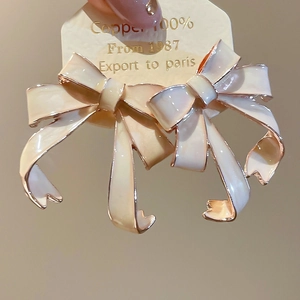 Close-up of cream enamel bow earrings with rose gold edges on a display card
