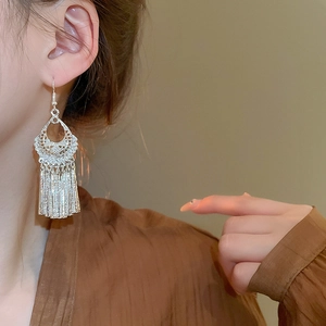 Detailed close-up of retro silver tassel earrings featuring intricate hollow carving on model