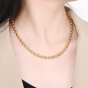Close-up of golden hollow bead chain necklace worn by a model in a beige suit