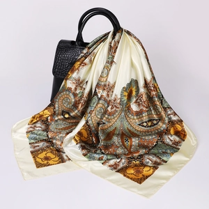 Detail of paisley silk scarf in champagne hue draped over a textured black leather handbag