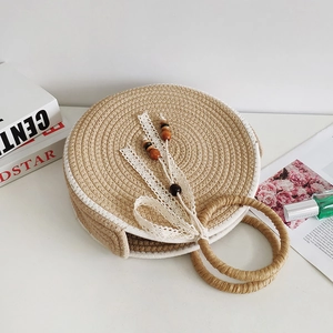 Minimalist round straw tote bag with lace bow and wood beads on a desk