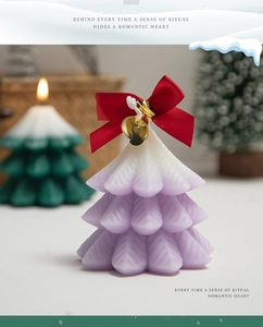 Macro detail of a purple gradient Christmas tree candle with a red bow and gold bell