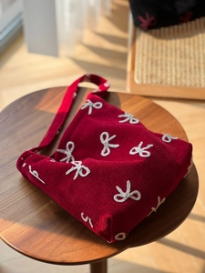 Detail of red corduroy shoulder bag featuring white bow embroidery on a wooden table