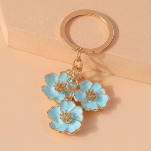 Close-up of golden keychain with three blue enamel peach blossom pendants on beige background