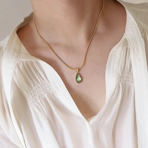 Detail of green teardrop pendant on gold snake chain worn over a white blouse