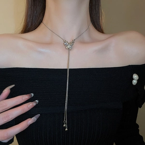 Detail view of a silver butterfly tassel necklace worn on a black elegant outfit