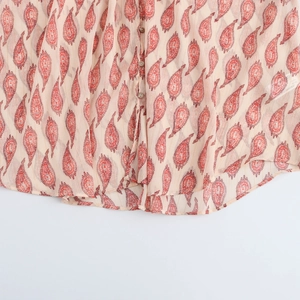 Detail of red paisley print on beige chiffon shirt with front buttons and stitching