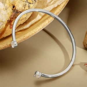 Minimalist silver open cuff bracelet with two clear zircons on a natural stone background