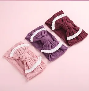 Detailed knit texture of three infant headbands with bows and white pom-pom edges