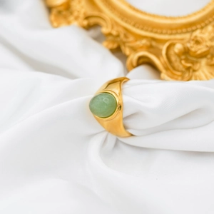 Detailed view of an 18k gold-plated ring featuring a green oval agate on white satin