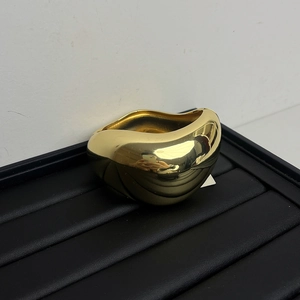 Detailansicht eines goldfarbenen geometrischen Wellenarmreifs auf einem schwarzen Tablett