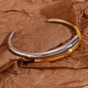 Detail of two-tone crossover bangle in gold and silver finish on textured paper