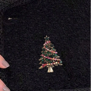 Sparkling Christmas tree brooch for women with green crystals on a black fabric background