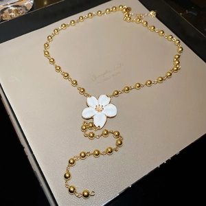 Detail of elegant gold beaded necklace featuring a white enamel flower pendant