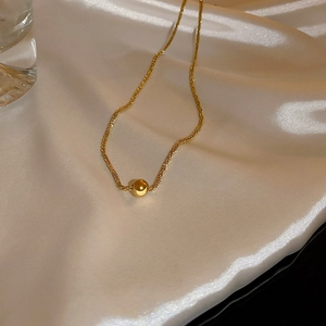 Dettaglio collana minimalista con perline dorate su seta bianca con eleganti accessori