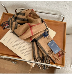 Detail of camel plaid scarf with red stripes and fringe edges on a wooden tray