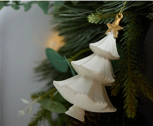 Close-up of cream-white Christmas tree ornament with gold star on pine branches