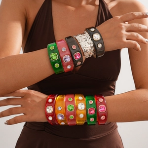 Close-up of stacked colorful resin bangles with inlaid gemstones and metallic textures