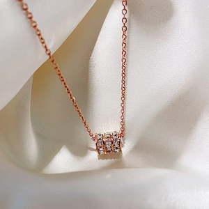 Close-up of a rose gold necklace with a crystal-encrusted cylinder pendant on white silk
