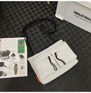 White nylon messenger bag featuring dual front drawstring pockets and orange side label detail