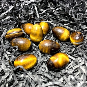 Polished tiger eye egg stones with golden stripes on black decorative raffia background
