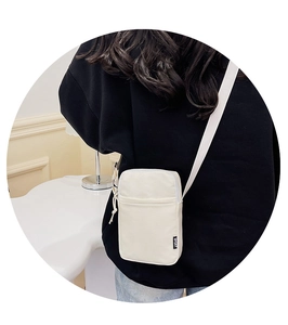 Close-up of a white canvas crossbody bag featuring a SPORT tag and adjustable strap
