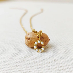 Detailed macro view of gold letter C pendant with small white pearls on textured fabric
