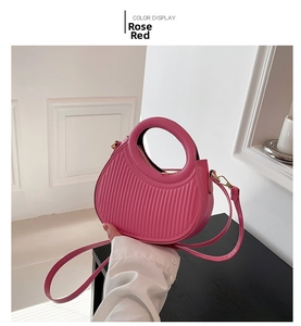 Detail of rose red crescent bag showing vertical pleated texture and round hollow handle
