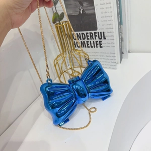 Detail of a shiny blue metallic bow-shaped evening clutch with a fine gold chain strap
