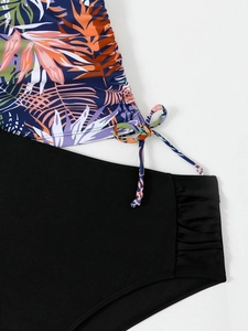 Detail of tropical leaf print tankini top with side drawstring and black bikini bottoms