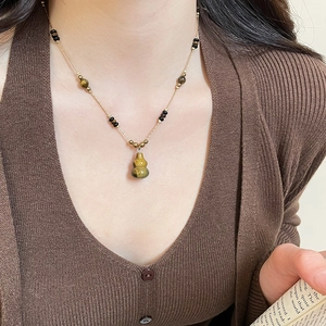 Close-up of a vintage tiger eye stone gourd pendant on a gold chain worn by a model