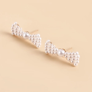 Detailed macro of handcrafted faux pearl bow earrings with golden finish metal accents