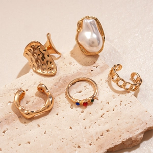 Detail of 5-piece gold geometric ring set with pearl and rhinestones on beige stone