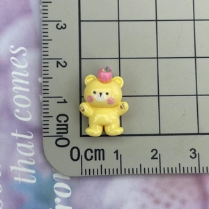 Macro view of a 2cm yellow resin bear figurine with apple and ruler for scale