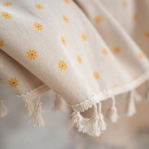 Close-up of linen table cloth with yellow daisy patterns and elegant white fringe