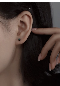 Détail macro d'une boucle d'oreille carrée vert foncé minimaliste portée à l'oreille