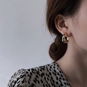 Close-up of golden C-shaped lava texture metal earrings worn on a model's ear