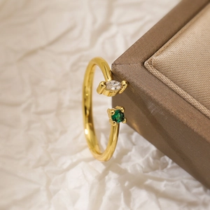 Macro detail of gold-plated open ring featuring marquise white and round green stones