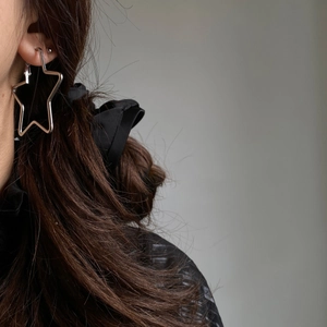 Close-up of minimalist silver star hollow hoop earring worn by a model in soft lighting