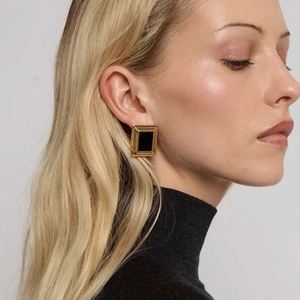 Close-up of elegant square black onyx earrings with gold plating on a model's ear